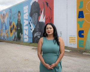 Mas Cultura Founder Posing In Front Of Wall Of Murals For Jayce Carmelo Luevanos, Uziyah Garcia, Eliahna Torres, And Jose Manuel Flores — Alfredo Rendón