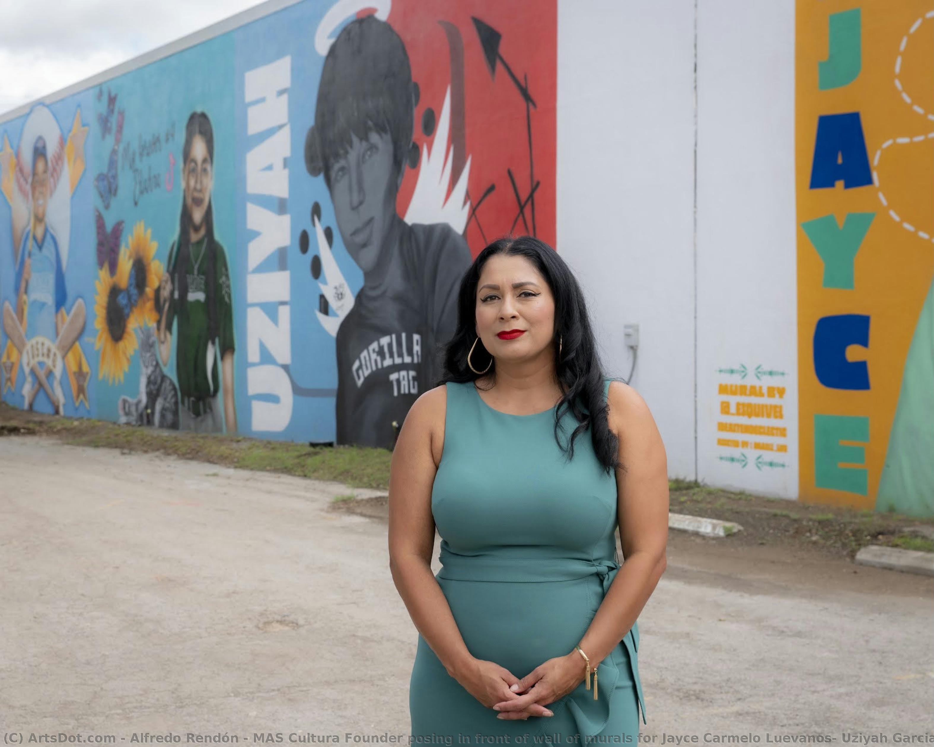 MAS Cultura Founder posing in front of wall of murals for Jayce Carmelo Luevanos, Uziyah Garcia, Eliahna Torres, and Jose Manuel Flores